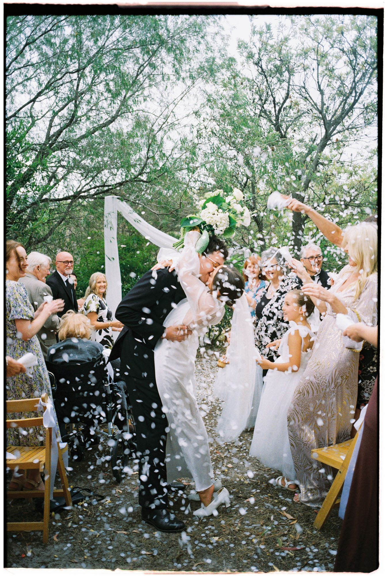 intimate backyard wedding ceremony bride and groom having a dip kiss down the aisle with confetti on 35mm film